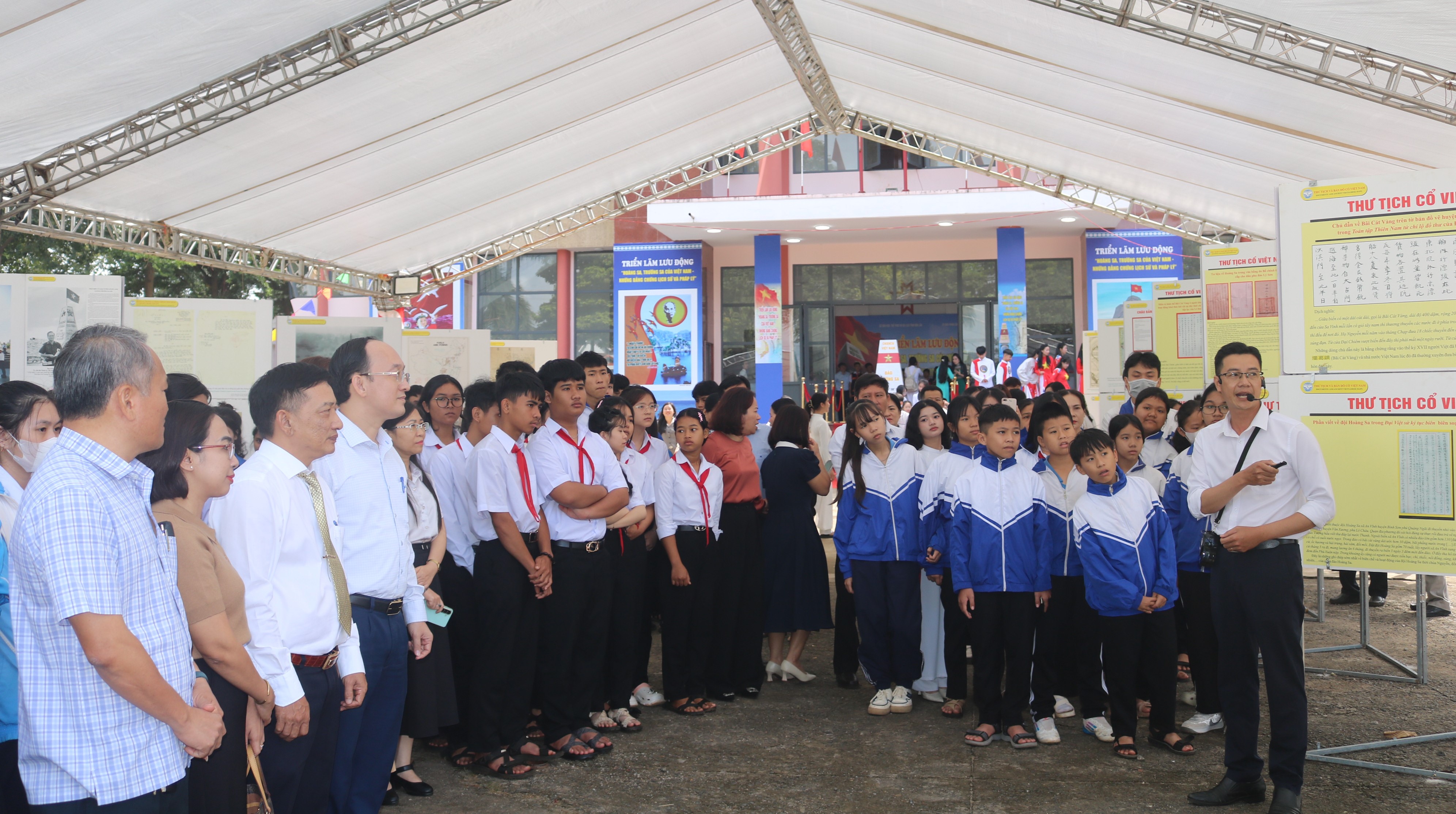 Đại biểu và các em học sinh nghe thuyết minh nội dung các tư liệu được trưng bày tại Triển lãm